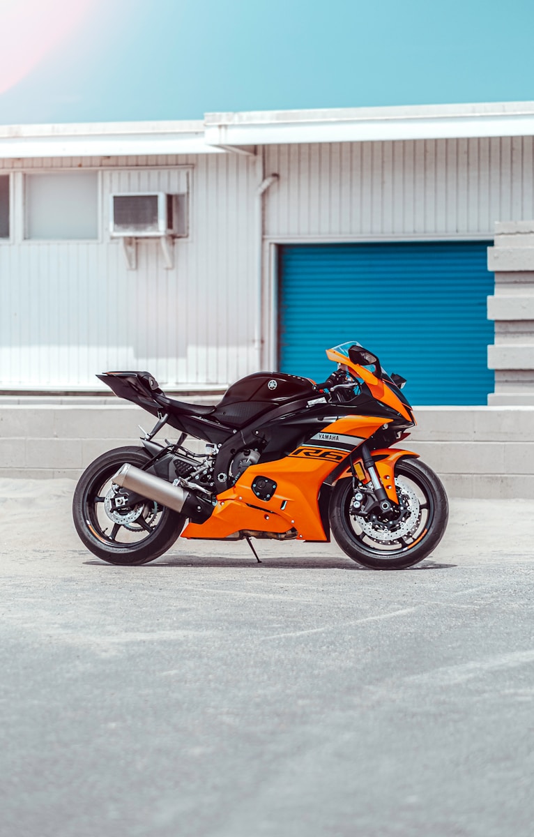 orange and black sports bike parked beside blue and white building